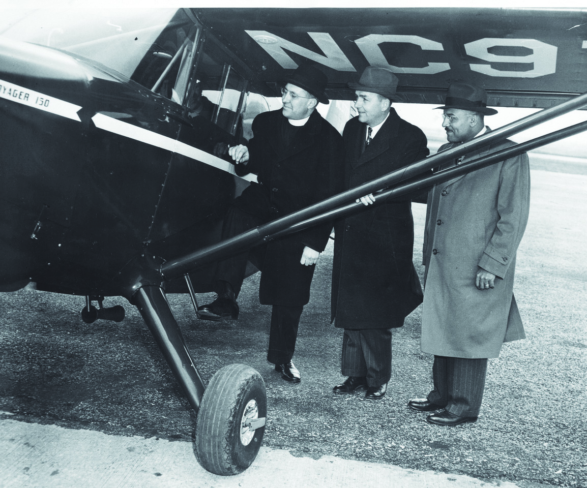 vintage photograph of three men—two White and one Black—in coats and hats standing next to a small airplane