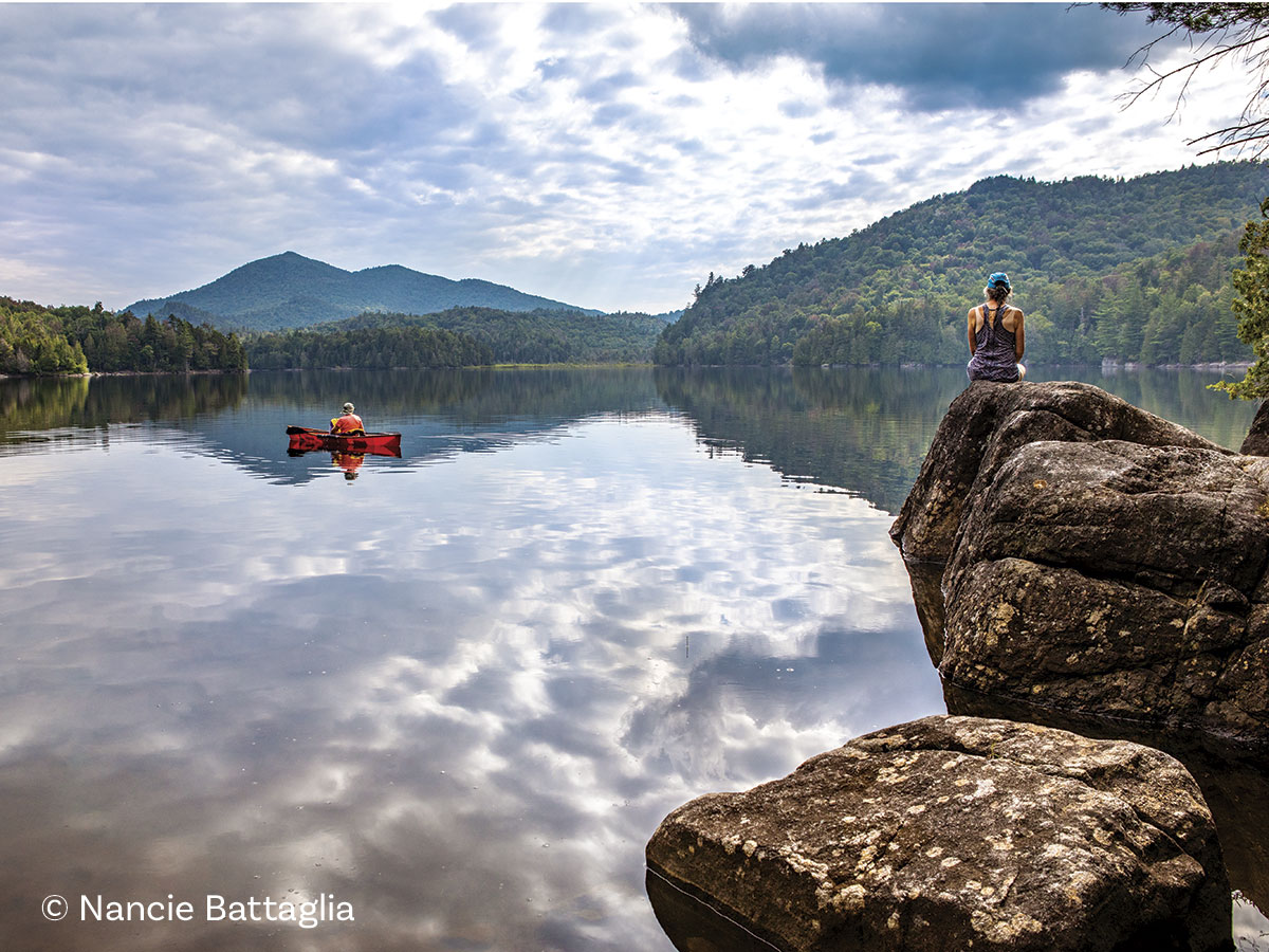 ja2022-nbNewcHendersonLk5-7110-web-1 woman sitting on a rock looking at a lake and mountains