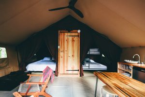 two beds and wood furniture inside a canvas tent.
